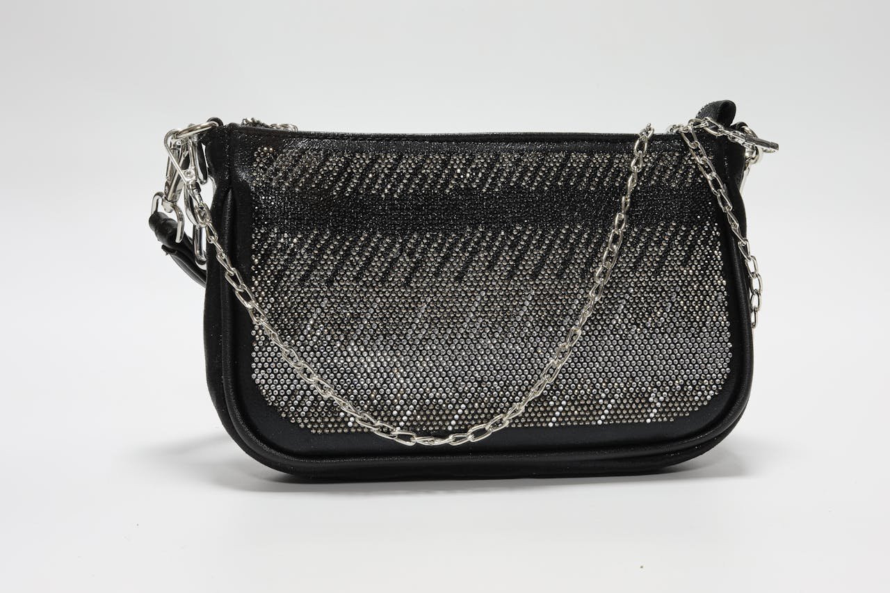 Stylish black handbag adorned with chain handle and rhinestones on a white background.