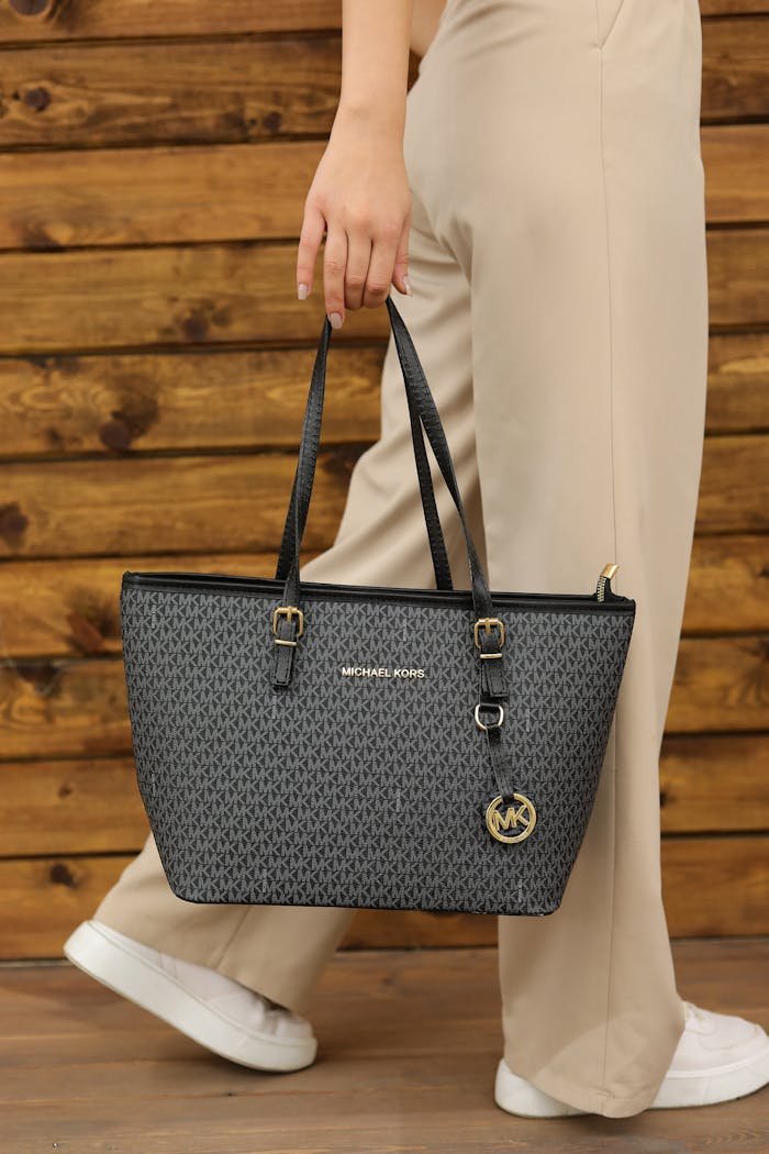 Elegant black tote bag held by a woman against a wooden backdrop.