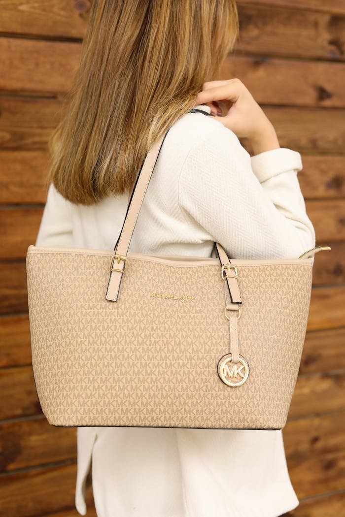 why-choose-us Elegant beige leather tote bag worn by a woman against a wooden backdrop.
