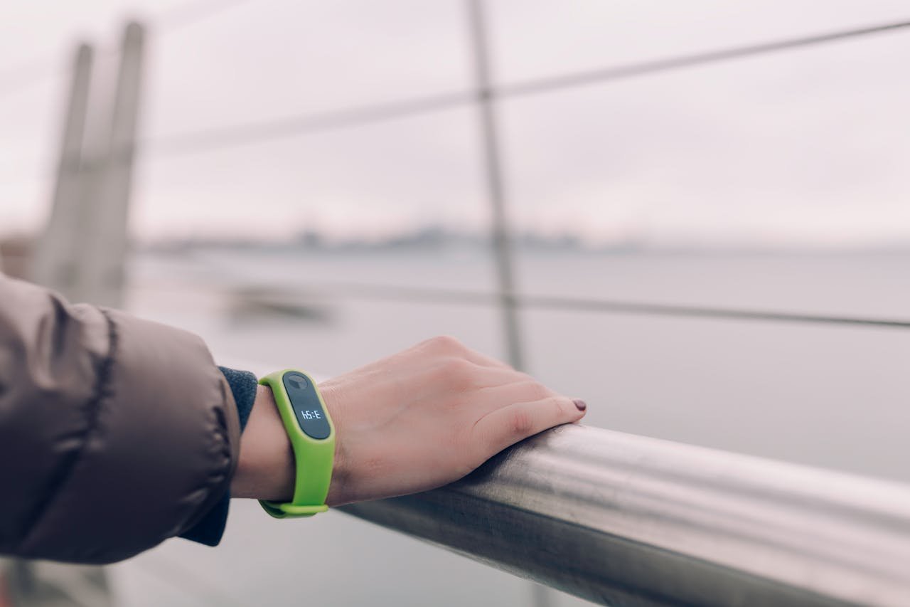digital A woman wearing a green smartwatch rests her hand on a railing with a blurred city skyline in the background.
